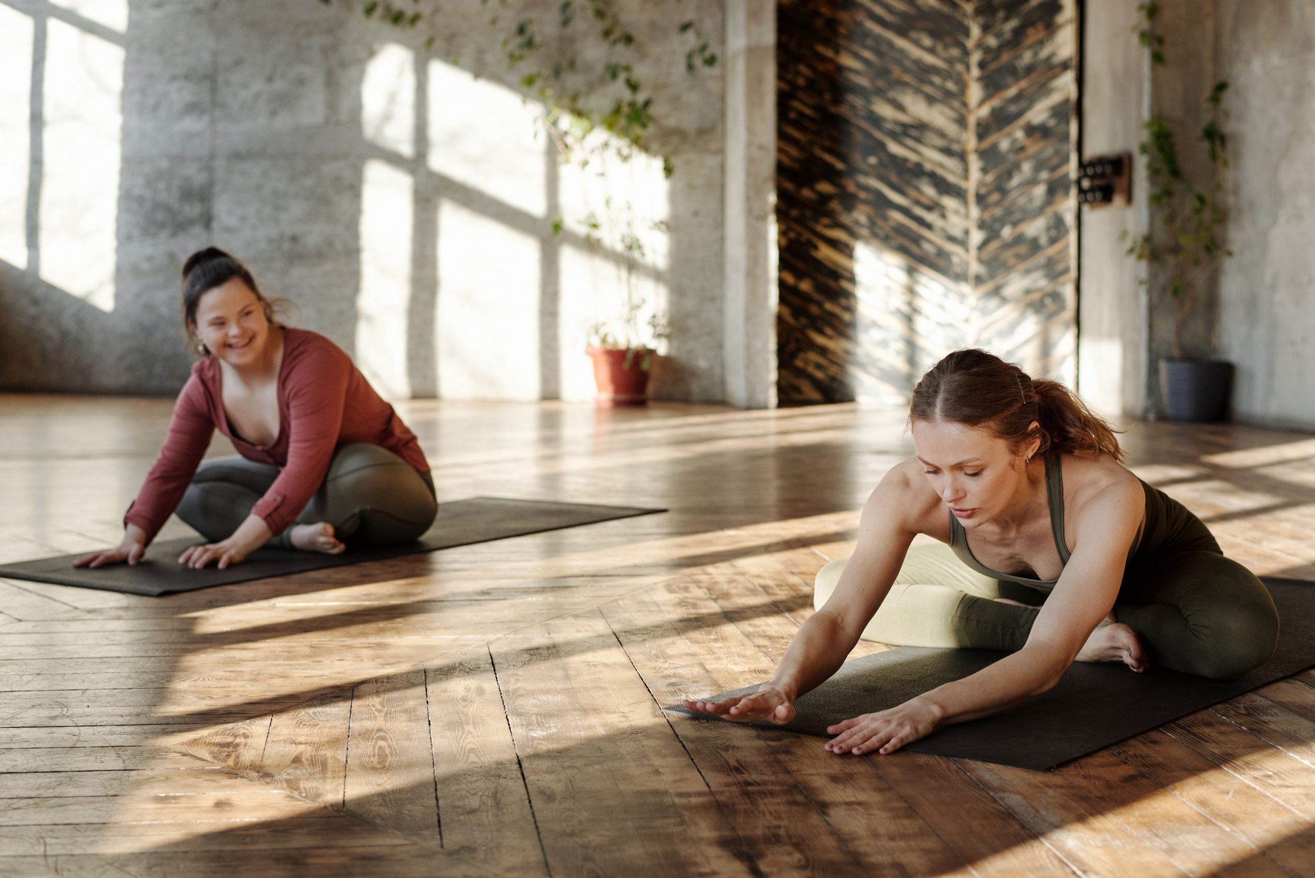A woman stretching on a wooden floor in a sunlit room