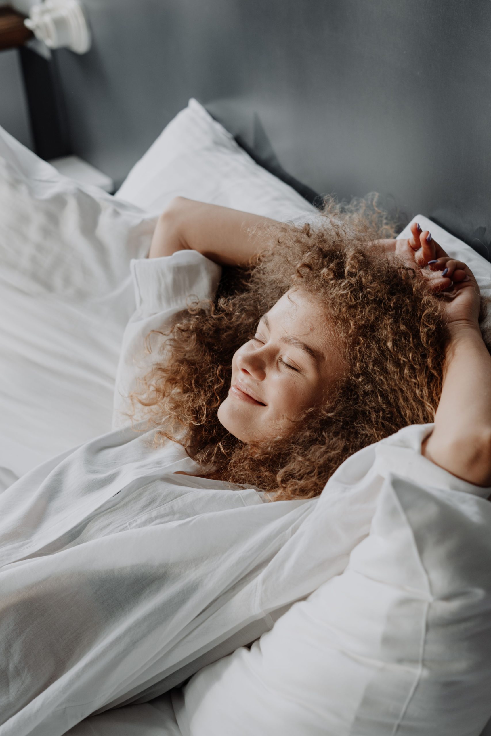 A woman waking in bed, stretching her arms above her head in morning light