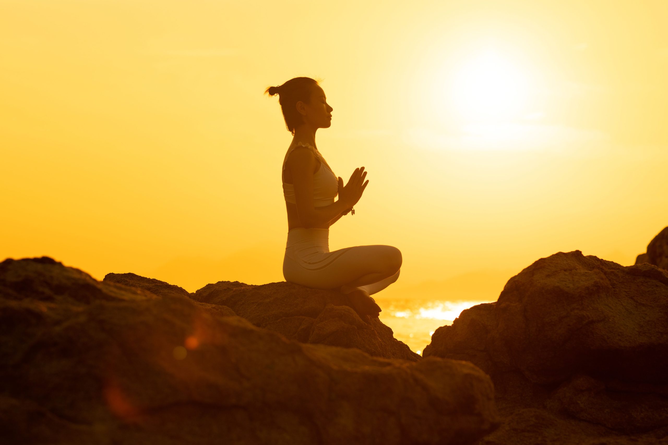 A person sitting cross-legged on a rock at sunset, hands together