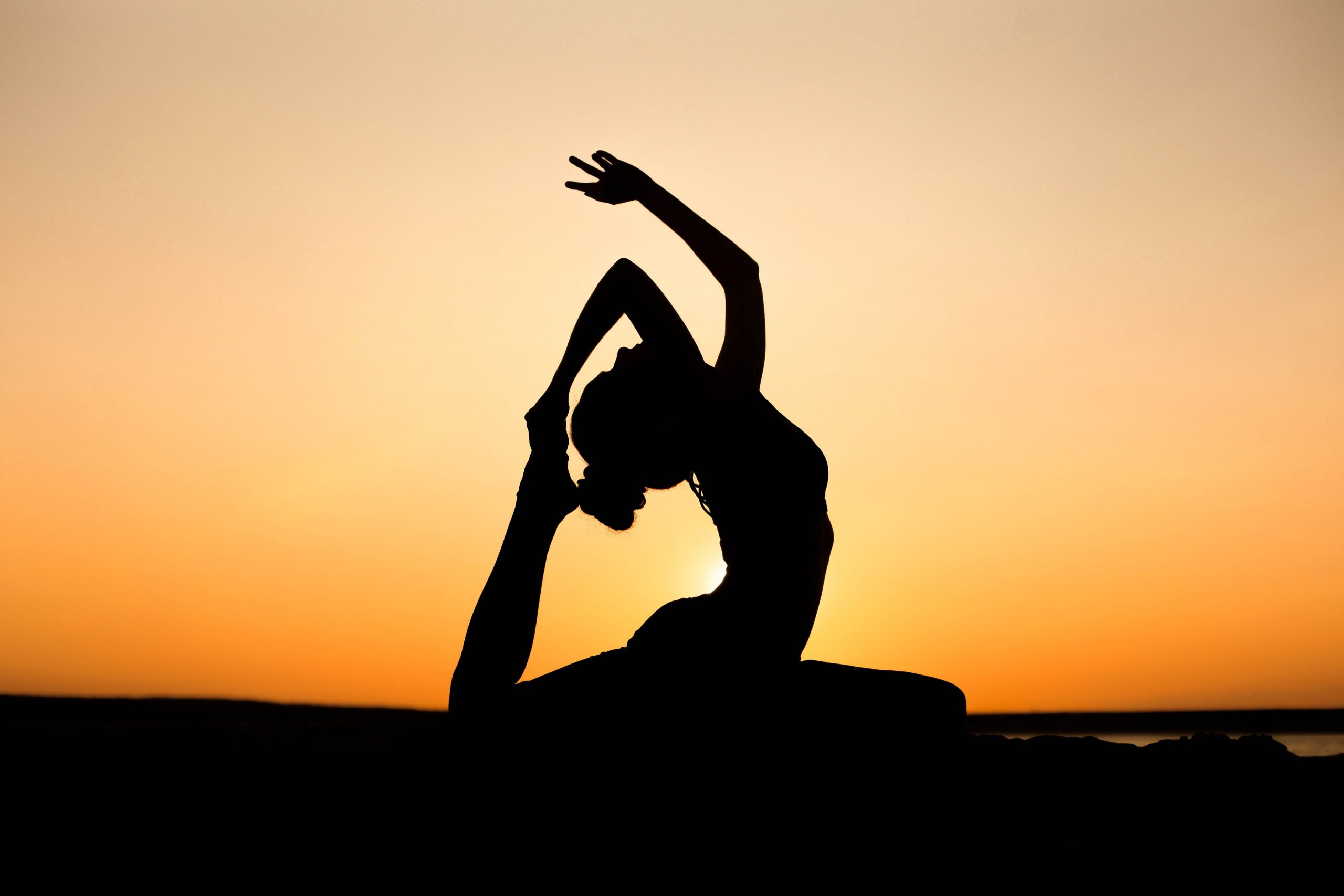 A person silhouetted in a backbend stretch against a sunset sky